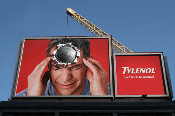 A billboard advertisement by Tylenol, displaying an image of a man holding his head in pain, and a wrecking ball appears to have hit the billboard right where the man's forehead is.