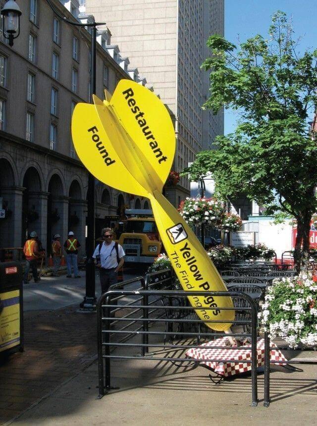 Displayed is a Yellow Pages ad, a large sculpture of a dart going into the ground with the Yellow Pages logo. 