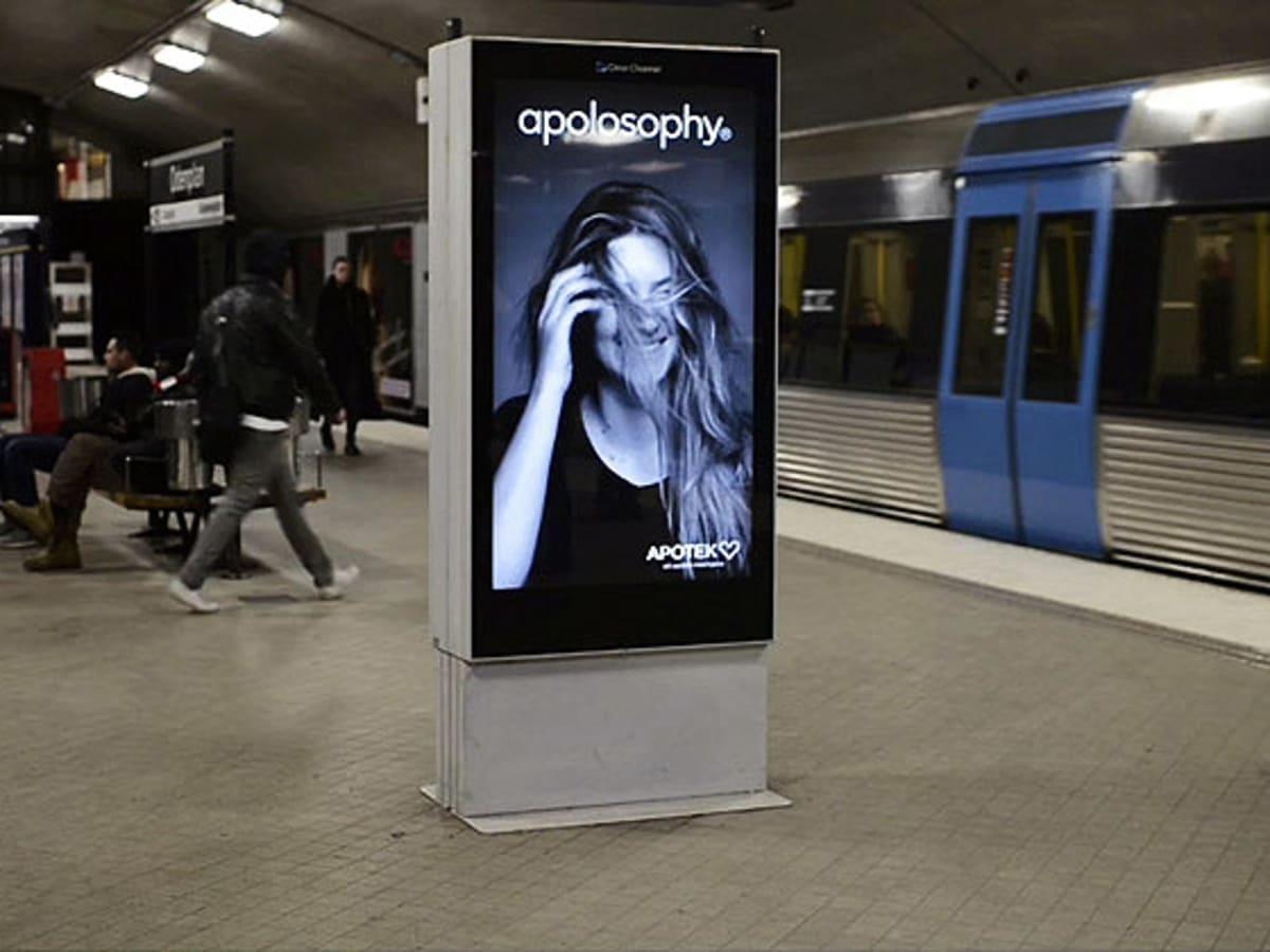 An digital advertisement board located in a subway station, displaying a woman's hair being blown around