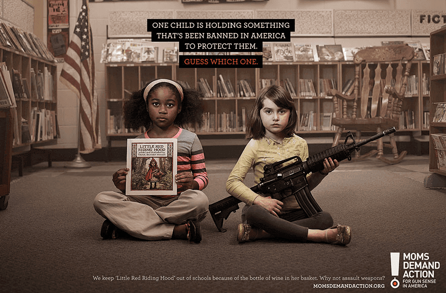 An ad by the organization Moms Demand Action, pictured is two children sitting in a library, one holding a book and the other a gun. Displayed above the children is text that reads, "One child is holding something that's been banned in America to protect them, guess which one".